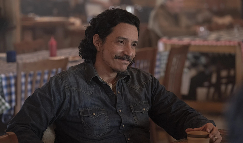 Tommy wearing a denim jacket, smiling while holding a ceramic mug sitting at a table.