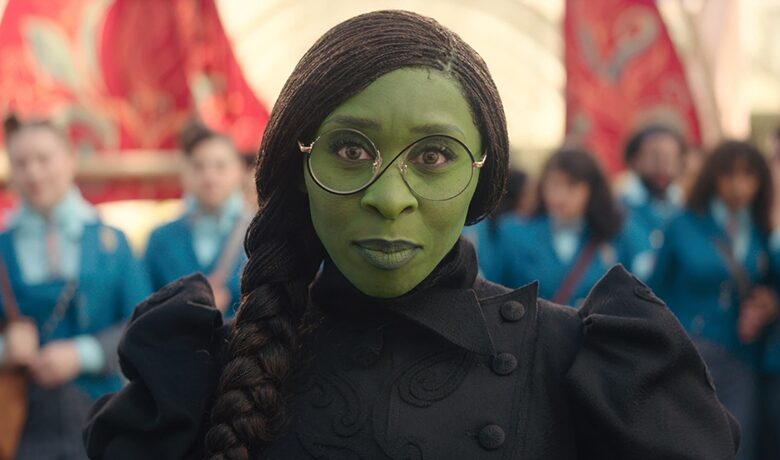 Le personnage Elphaba vêtu de noir avec une tresse dans les cheveux et des lunettes rondes.