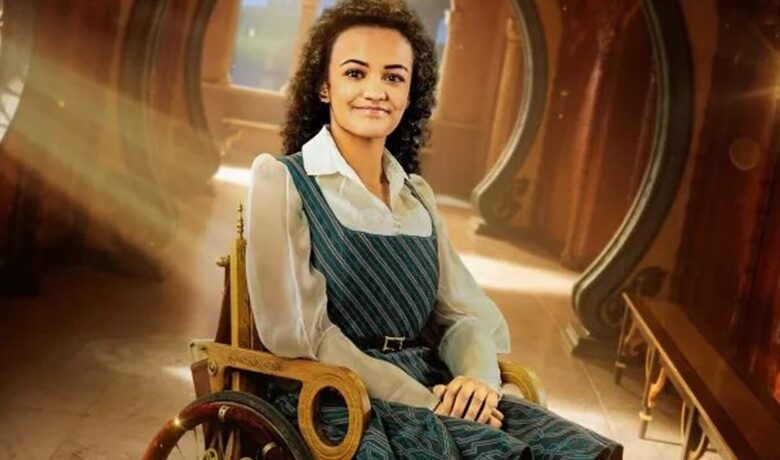 Le personnage Nessarose assis dans son fauteuil roulant en bois dans un couloir.