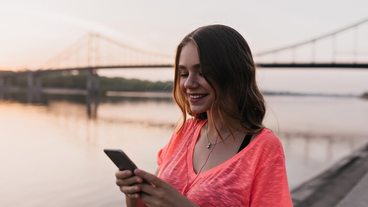 Mujer sonriendo mientras usa su teléfono celular vistiendo una blusa rosa