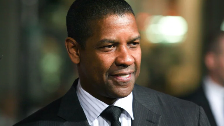 O ator Denzel Washington vestindo terno e gravata com um sorriso no rosto