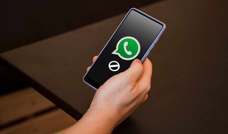 Mão segurando um celular com o símbolo o Whatsapp na tela junto a um sinal de bloqueado