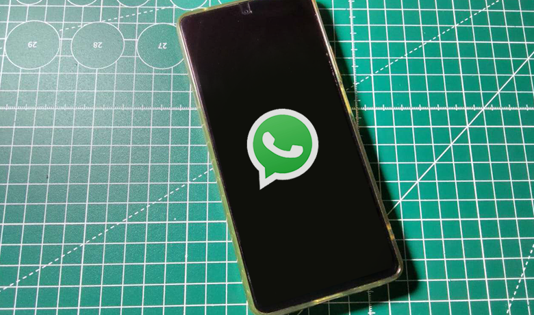 Um celular ao centro de uma mesa verde com o símbolo do Whatsapp na tela