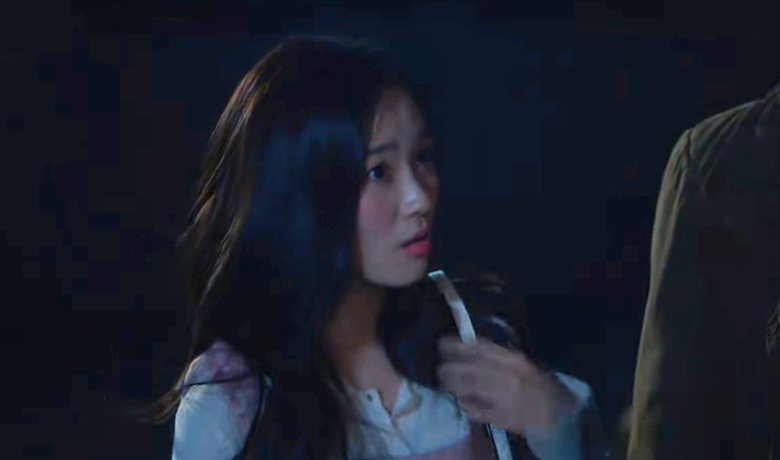 Garota de expressão surpresa aparece em cena noturna, com os cabelos soltos e camisa clara. Ela segura a alça da bolsa em um momento tenso.